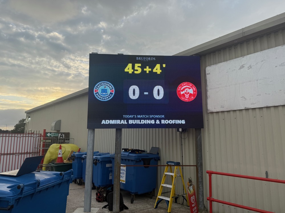 LED scoreboard at a football ground showing the match clock at dusk