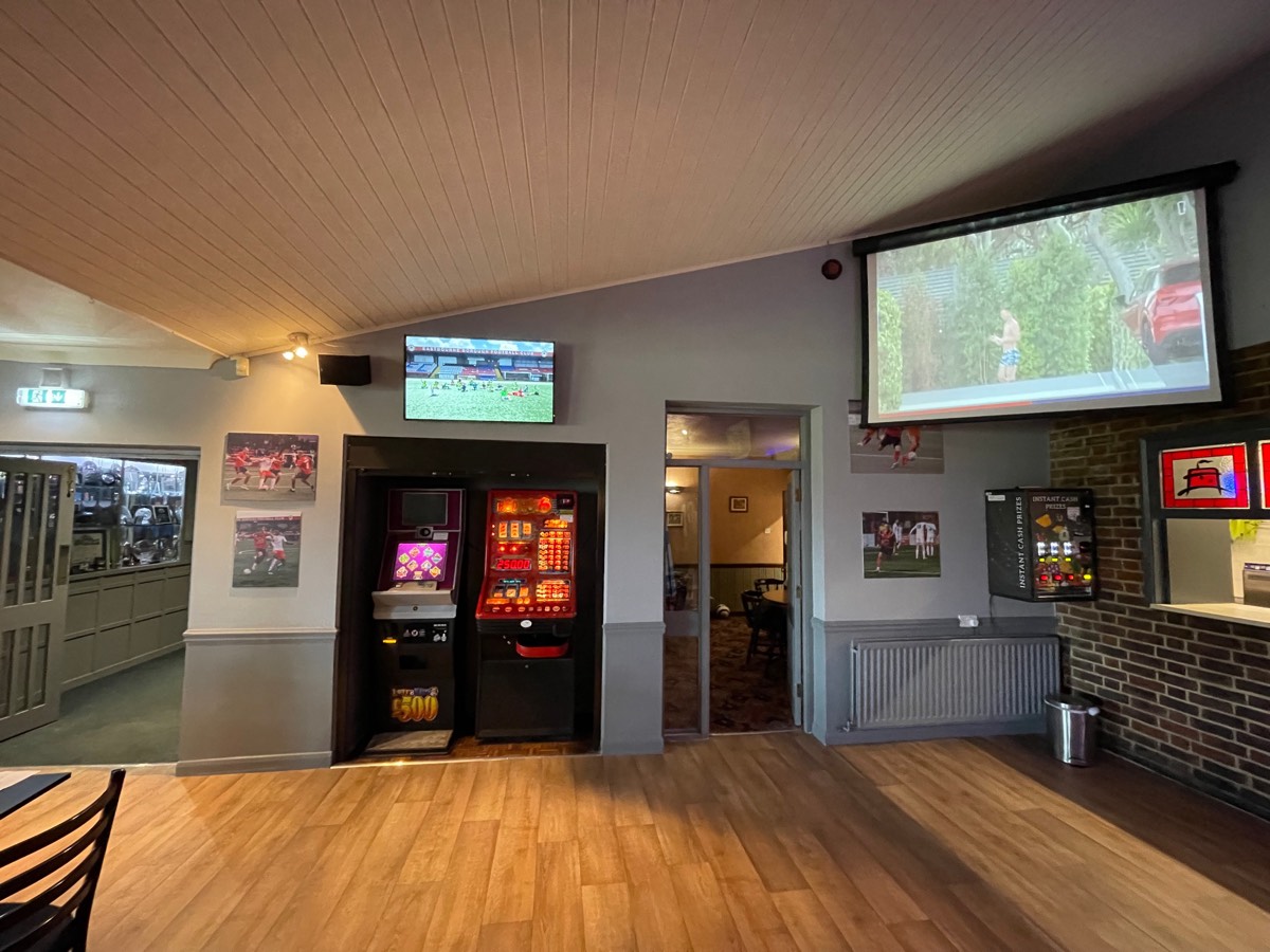 Wall-mounted screen showing live football beside a projector screen in a clubhouse