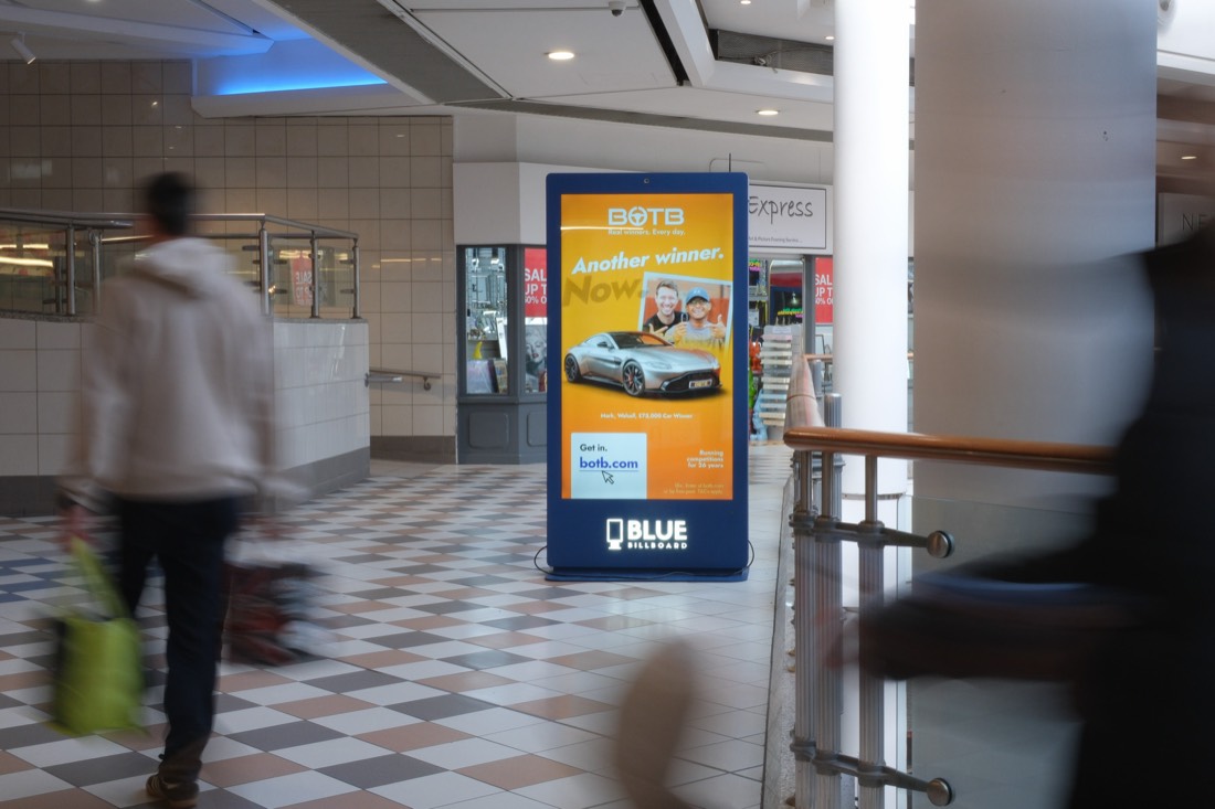 Digital advertising screen in a shopping centre with passing shoppers