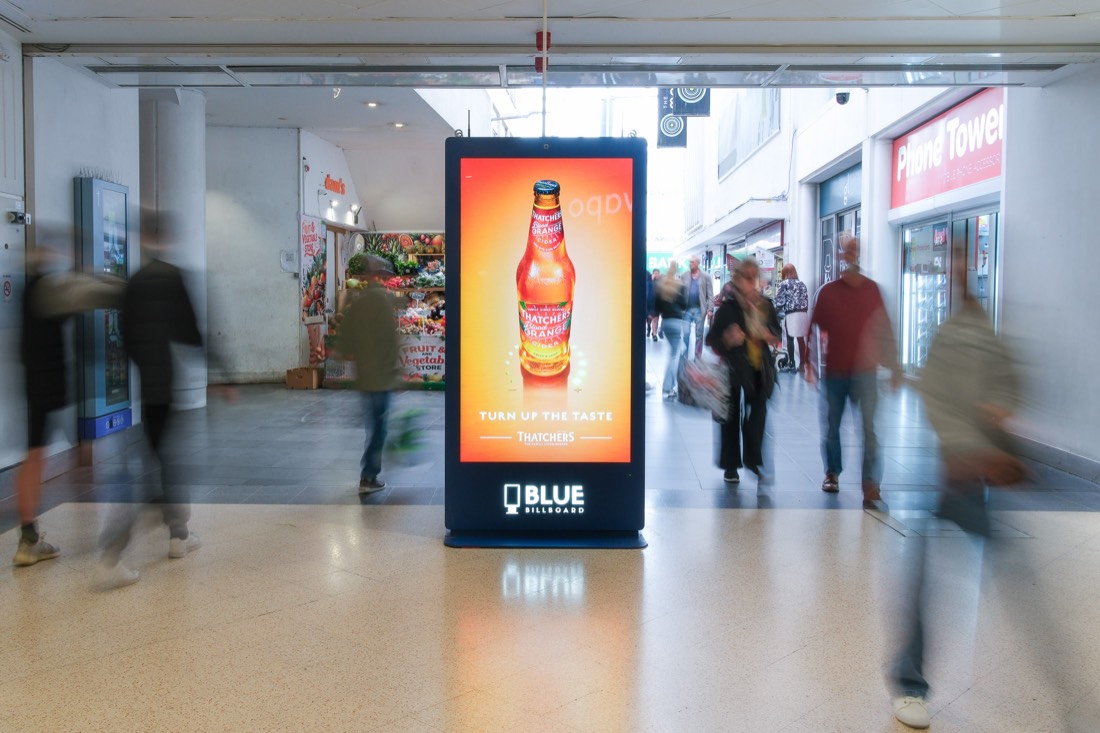 Digital promotional screen beside storefronts in a shopping mall